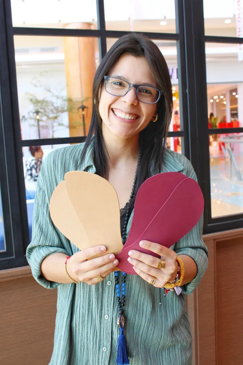 Gaby sonríe mientras sostiene dos figuras de papel con forma de corazón